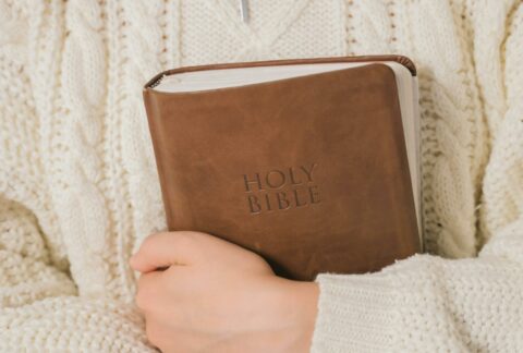 mulher vestindo sweater creme abraçando uma bíblia de capa marrom